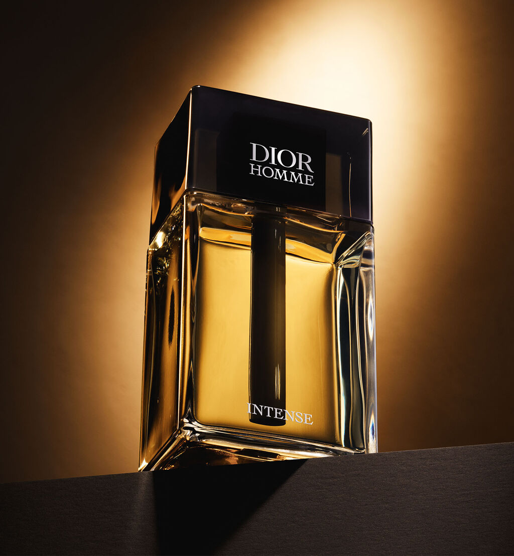 Dior Homme Intense perfume bottle on a dark surface with a warm light background

