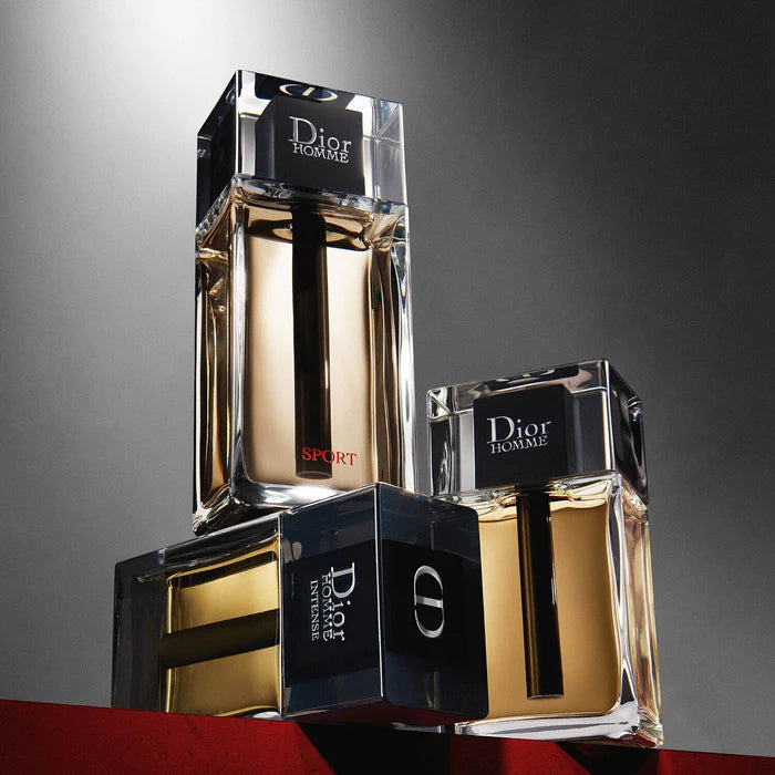 Three Dior Homme perfume bottles on a reflective surface with a gray background
